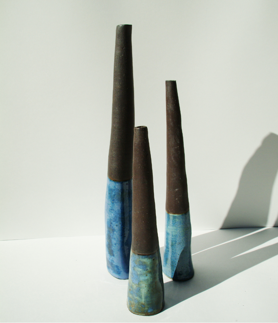 Group of tall ceramic vessels with striking two-tone glazing featuring dark brown upper sections and vibrant blue lower sections in varying heights