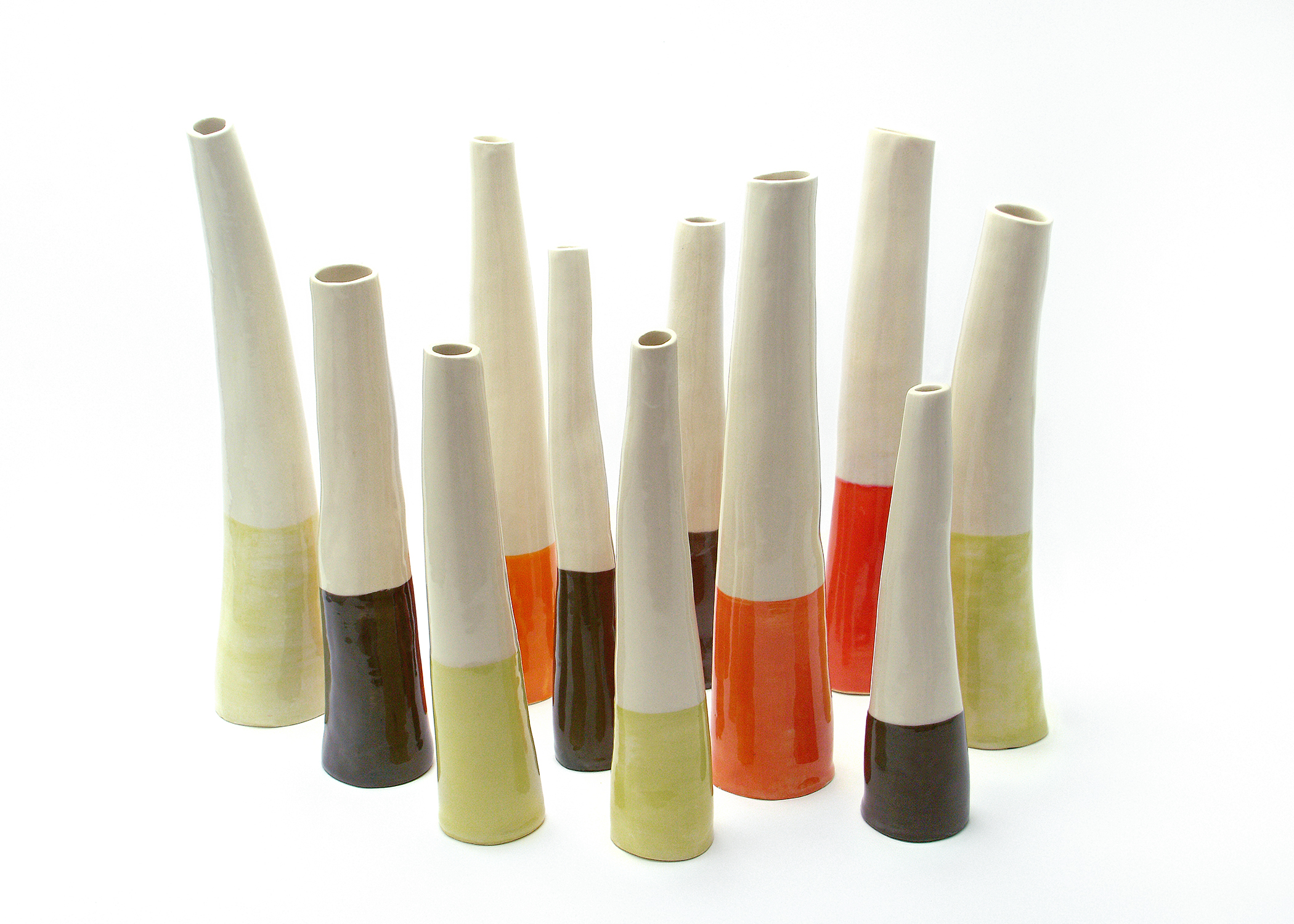 Collection of tall slender ceramic bud vases in various colors including orange, green, brown, and cream with modern two-tone color blocking