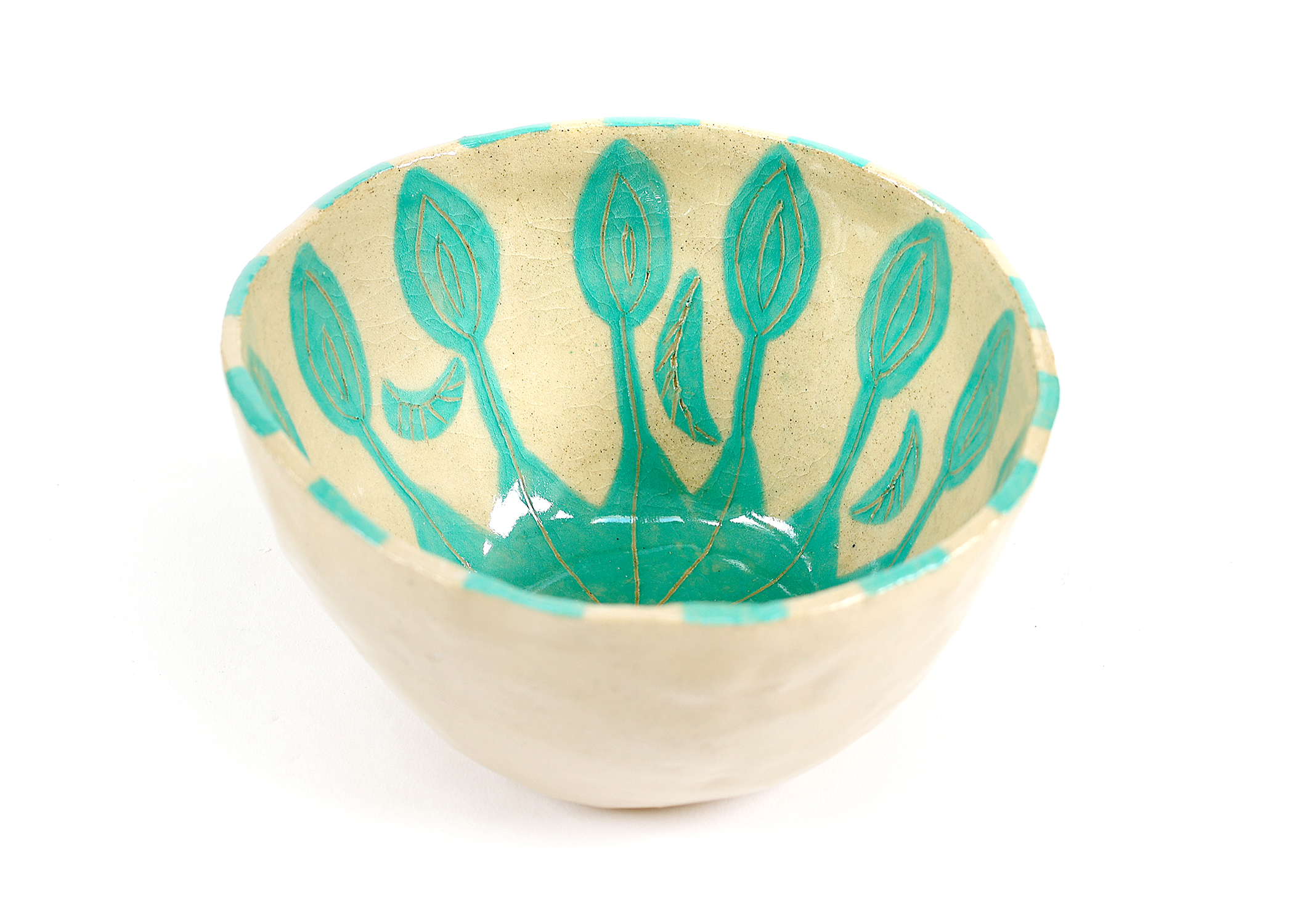 Ceramic bowl with turquoise leaf patterns on cream background, showcasing botanical motifs in coastal color palette
