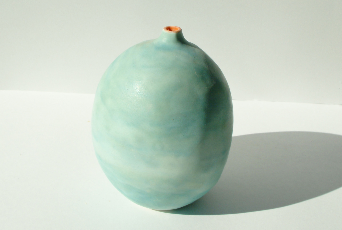Beautiful rounded ceramic vessel in soft turquoise and seafoam green with orange interior accent, showcasing organic coastal-inspired form