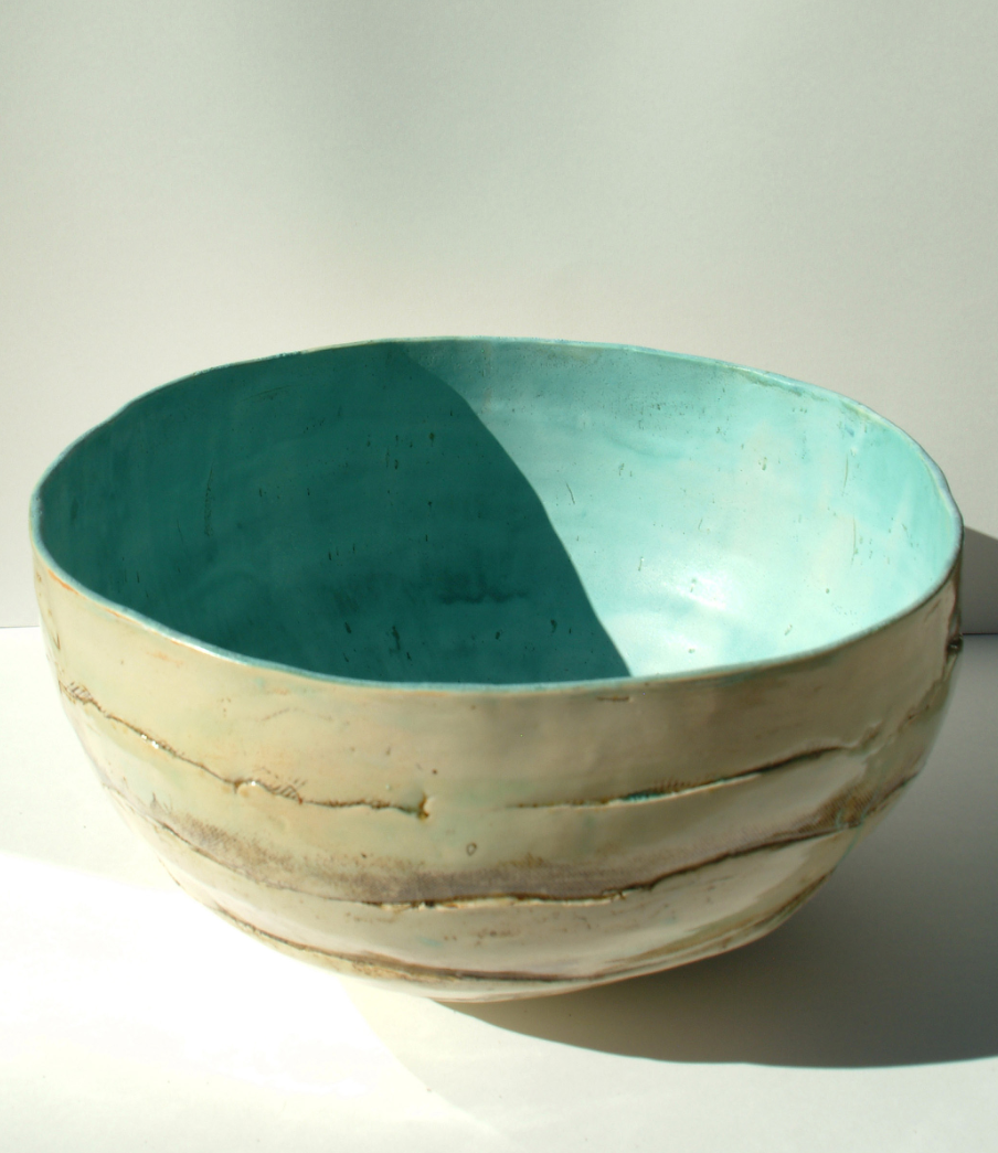 Ceramic bowl with cream exterior featuring horizontal ridged texture and stunning two-tone interior split between deep teal and lighter turquoise